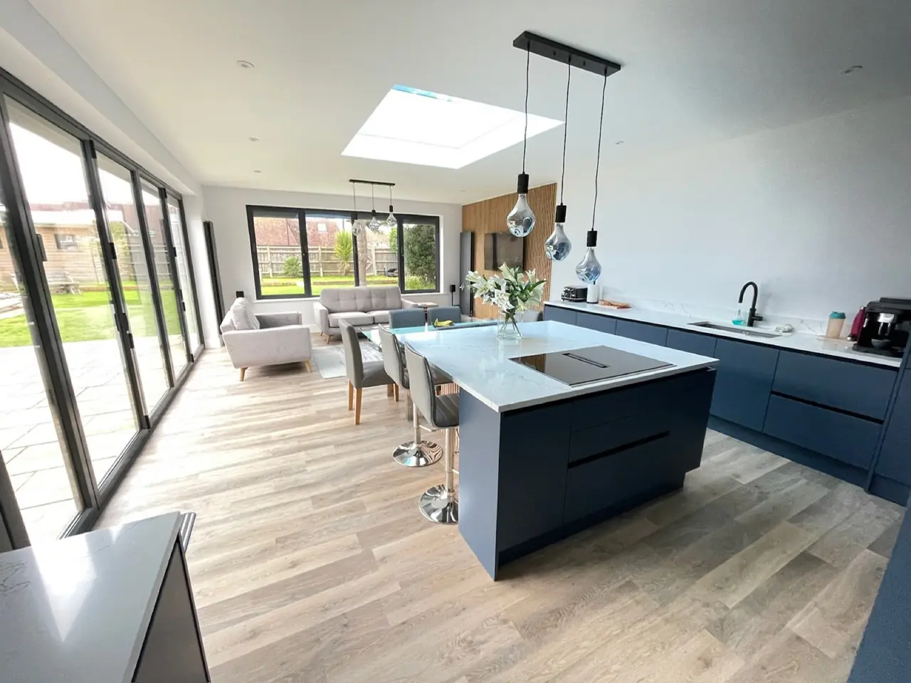 Open-plan navy blue fitted kitchen with a large island, skylight and bifold doors onto the garden